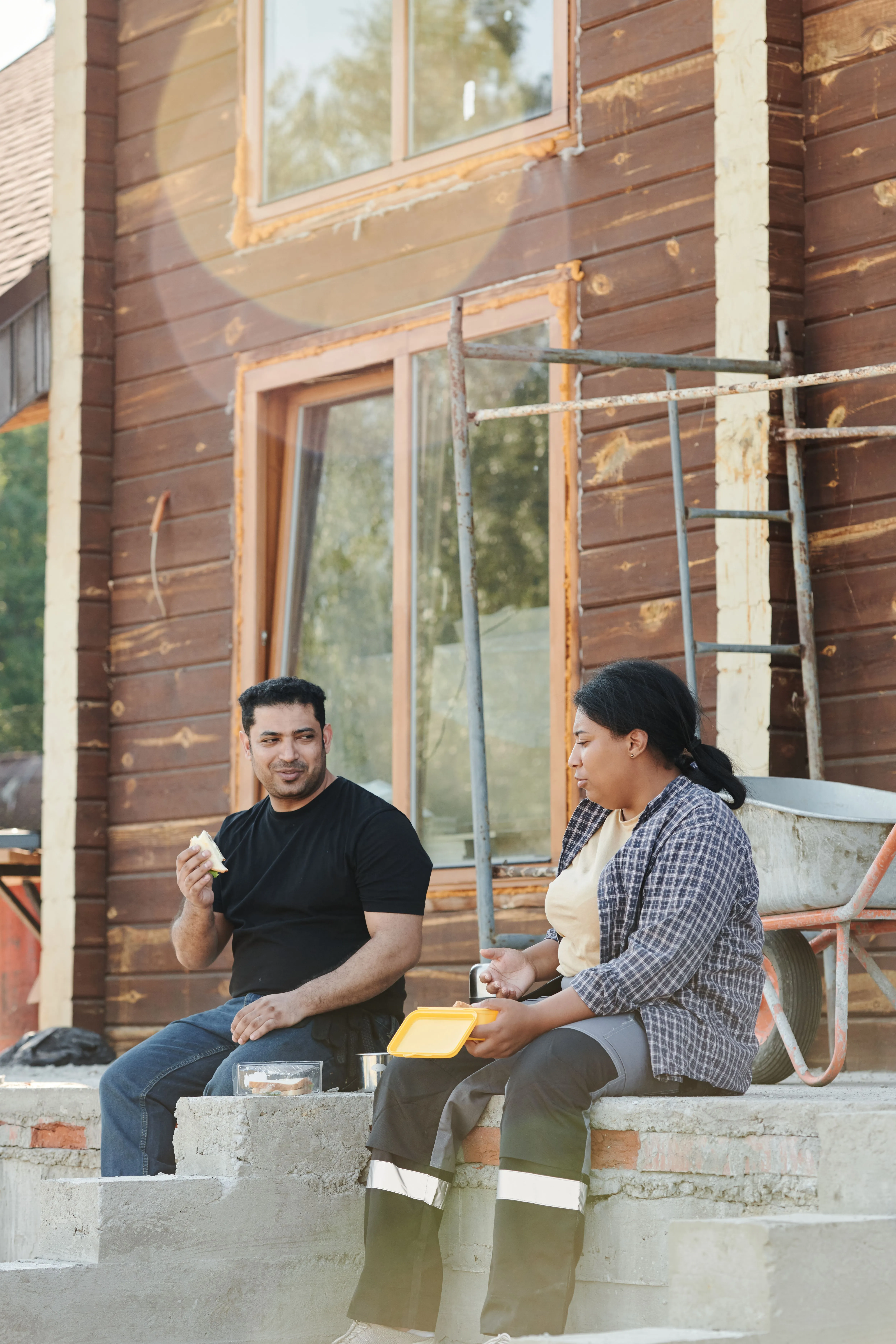 Dos personas conversan y comparten un almuerzo frente a una obra en construcción